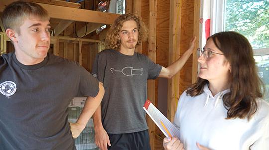 three students (woman, man, man, left to right) in tiny house