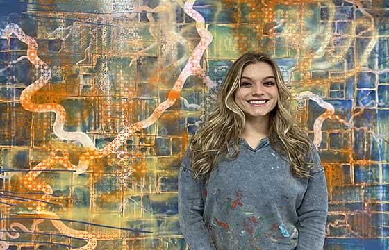 Jackie standing in front of highly patterned painting, smiling, hair down