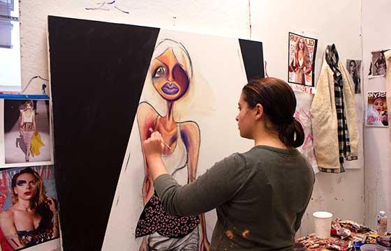 Carrie standing in studio, back to camera, painting large painting of woman