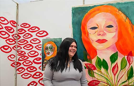 Alyssa standing in front of brightly colored painting of woman with orange hair, laughing and turning her face to the left