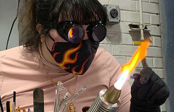 Abby with a blow torch, dark glasses and a face mask printed with flames