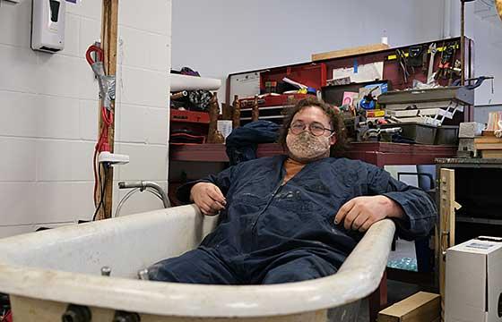 June sitting in cast iron bathtub wearing coveralls and lace mask