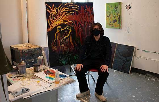 long haired and masked, Time sits on a stool in the studio