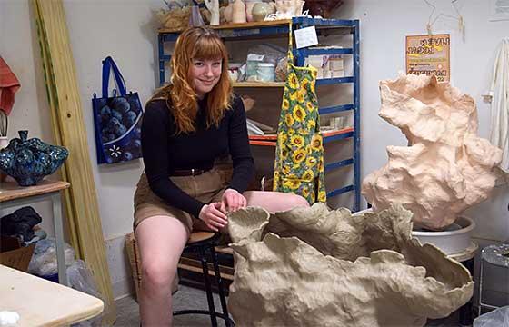 Sarah sitting on stool in her studio behind sculpture in progress